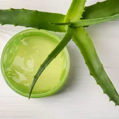 Zielony żel aloesowy w słoiczku, obok świeżych liści aloesu. Idealny aloes po opalaniu dla ukojenia skóry.