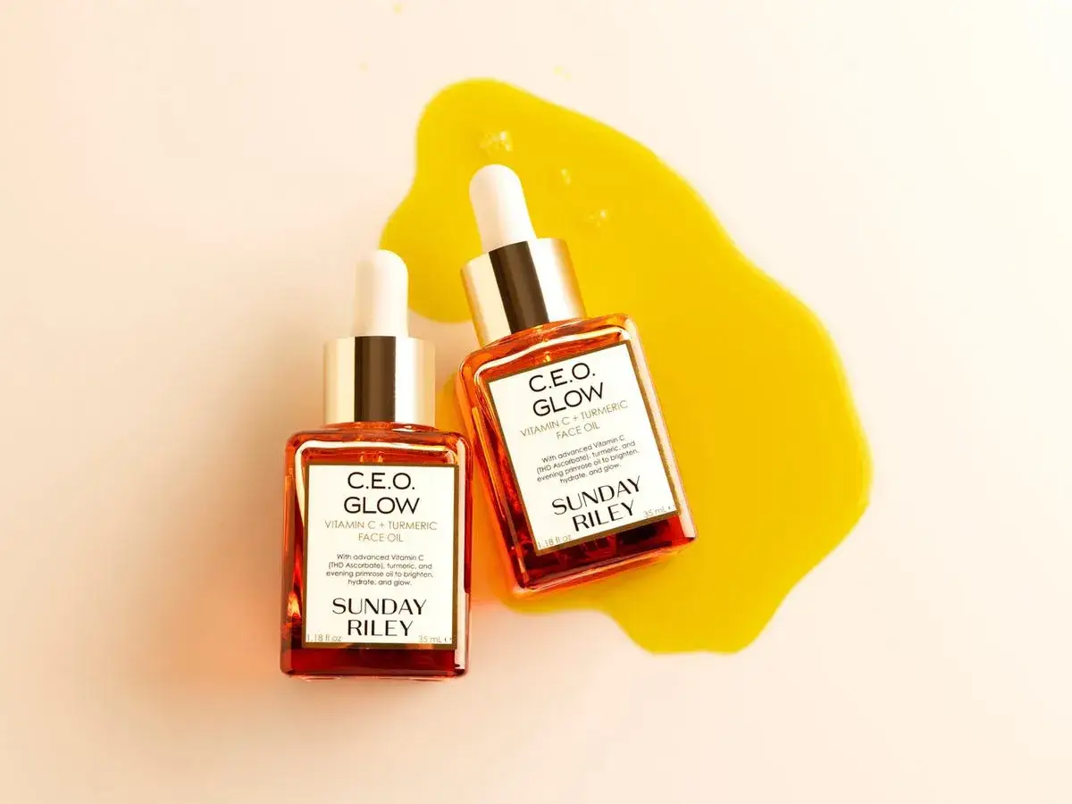 Dwa flakoniki serum C.E.O. Glow z witaminą C (w tym askorbylofosforan sodu) i kurkumą, otoczone złotym olejkiem.